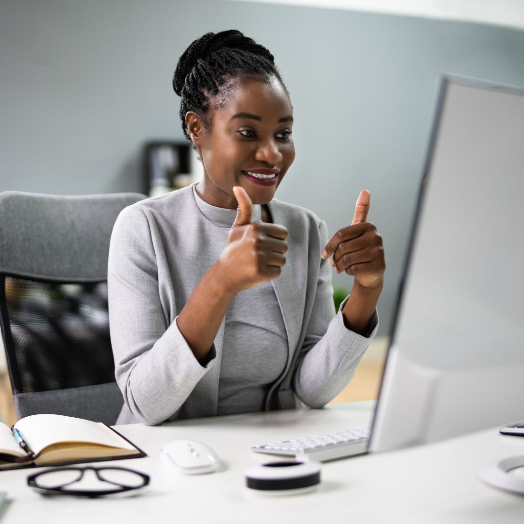 Happy leader sitting at desk in front of computer monitor giving thumbs up to Dr. Kevin John for a great leadership training.